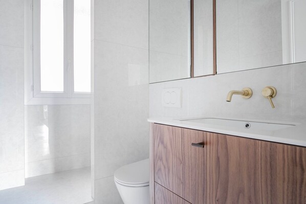A modern bathroom with a white toilet, a wooden vanity with a sink, and a mirror.