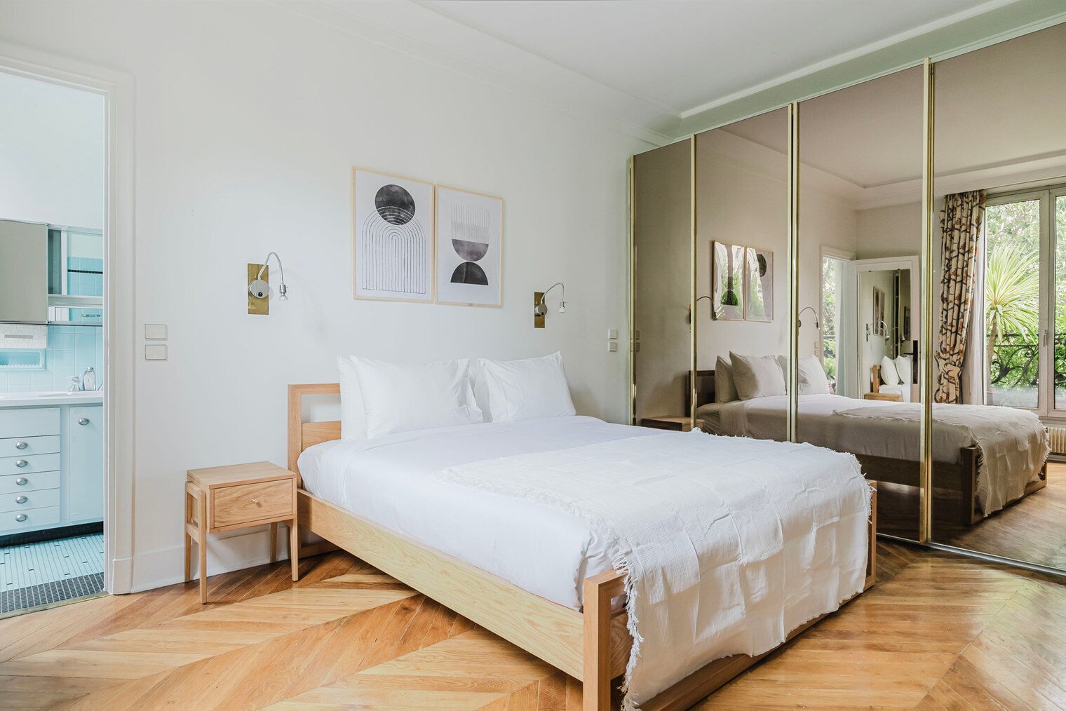 Un dormitorio con cama, mesita de noche, espejo y vistas al exterior.