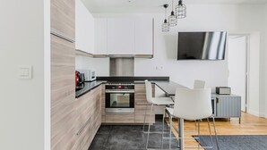 A modern kitchen with a built-in oven, a microwave, and a coffee machine. There is a dining area with a table and chairs.