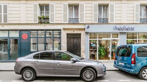 A gray sedan parked on a city street in front of a building with a storefront labeled "Precilens Centre de vision".