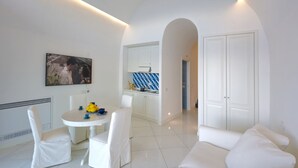 Un soggiorno moderno con un divano bianco, un tavolo da pranzo con sedie e un angolo cottura con mobili bianchi e piastrelle blu.
