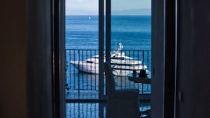 Vista attraverso una porta su un balcone con vista sul mare, con un'imbarcazione ormeggiata nelle vicinanze.