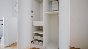 A white metal wardrobe with multiple shelves and drawers, a small electrical box on the top shelf, and a metal handle on the door.