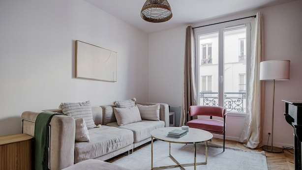 A modern living room with a sofa, a red chair, a coffee table, and a large window with curtains.