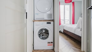 A laundry room with stacked washing machines and a bed in the adjacent room.