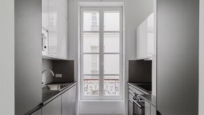 A narrow kitchen with white cabinets, a stainless steel sink, and an oven. - Blueground | Le Marais-Republique, nr restaurants (Paris)
