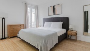 A bedroom with a bed, a nightstand, a dresser, a mirror, and a window with curtains. - Blueground | Le Marais-Republique, nr restaurants (Paris)