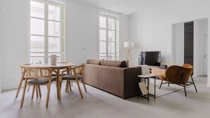 A modern living room with a sofa, a TV, a dining table with chairs, and a lamp. - Blueground | Le Marais-Republique, nr restaurants (Paris)