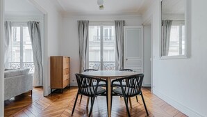 A dining area with a wooden herringbone floor, a round table, and four black chairs. - Blueground | Porte Dauphine, elevator & washer (Paris)