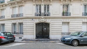 A building with a large black ornate entrance door, multiple windows with shutters, and balconies with black wrought iron railings. - Blueground | Porte Dauphine, elevator & washer (Paris)