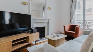 A modern living room with a flat-screen TV, a fireplace, a red armchair, and a large window with patterned curtains. - Blueground | Porte Dauphine, elevator & washer (Paris)