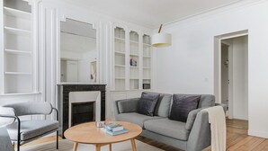 Ein modernes Wohnzimmer mit grauem Sofa, einem runden Holztisch, einem grauen Sessel und einem Kamin.