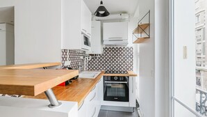 Eine kleine Küche mit weißen Schränken, einer Holz Arbeitsplatte, einem Einbauofen und einer gemusterten Spritzschutzleiste.