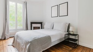 Ein Schlafzimmer mit Bett, Nachttisch, Lampe, Kamin und zwei gerahmten Bildern an der Wand.