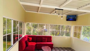 A sunroom with a red sectional sofa, a small table, and a TV mounted on the wall.