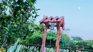 A garden with a wooden swing set and a small wooden structure.