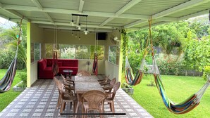 A covered patio with a dining table, chairs, a red sofa, and hammocks.