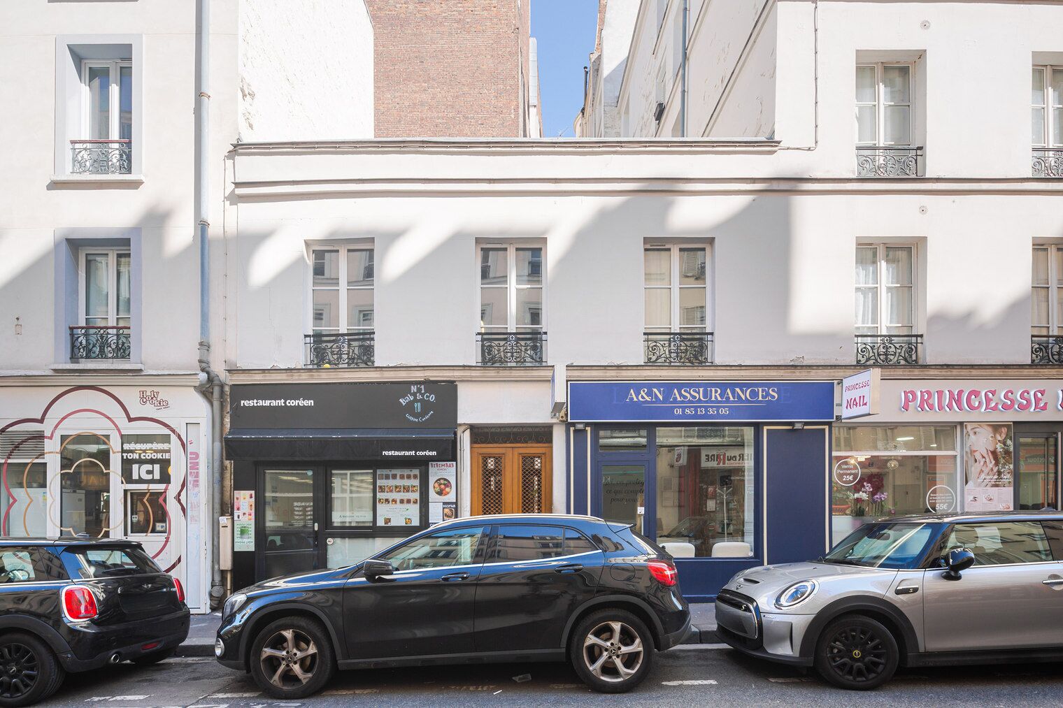 Vista de la calle con coches aparcados, una panadería, un restaurante y una oficina de seguros.