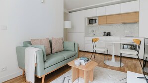 A modern apartment with a green sofa, a small wooden table, and a white kitchen with wooden cabinets.