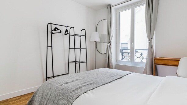 A hotel room with a bed, a wardrobe, a mirror, and a window with curtains.