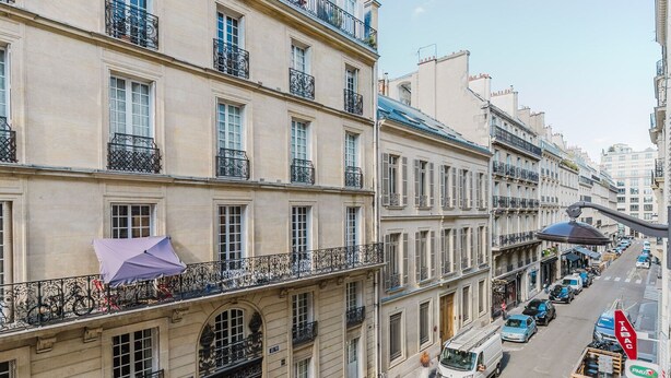 A multi-story building with balconies, a street view, and parked vehicles.
