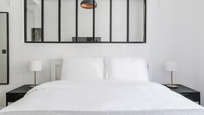 A modern hotel room with a large bed, two bedside tables with lamps, and a large mirror on the wall.