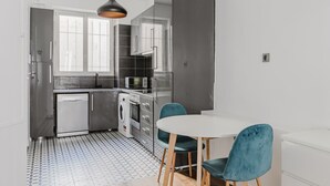 A modern kitchen with a dishwasher, microwave, and oven. There is a dining area with a white table and teal chairs.