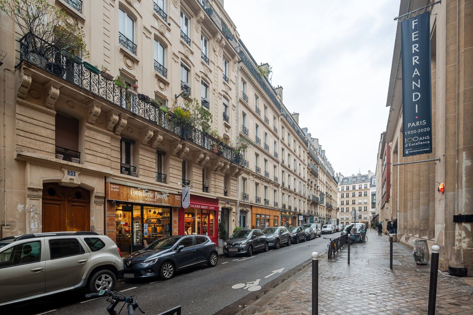 A street with parked cars and a building with a sign reading "FERRANDI PARIS 1920-2020 100 ANS d'Excellence".