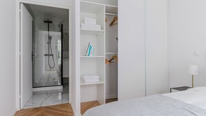 Et moderne hotelværelse med walk-in-skab, bruseområde og en fint redt seng.