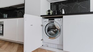 Et kompakt, moderne køkken med indbygget vaskemaskine og tørretumbler, trægulv og en backsplash i sort marmor.