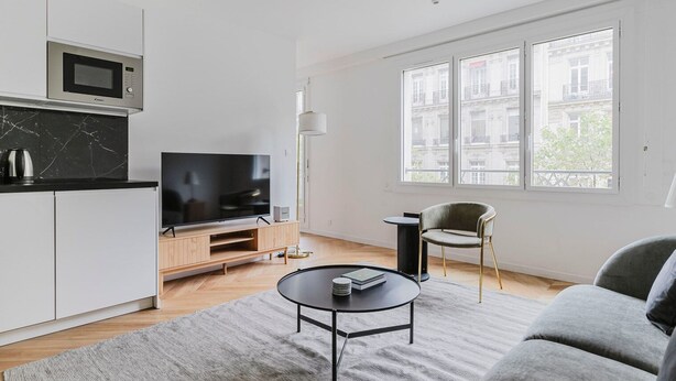 En moderne stue med et fladskærms-tv, et lille rundt bord og en sofa.