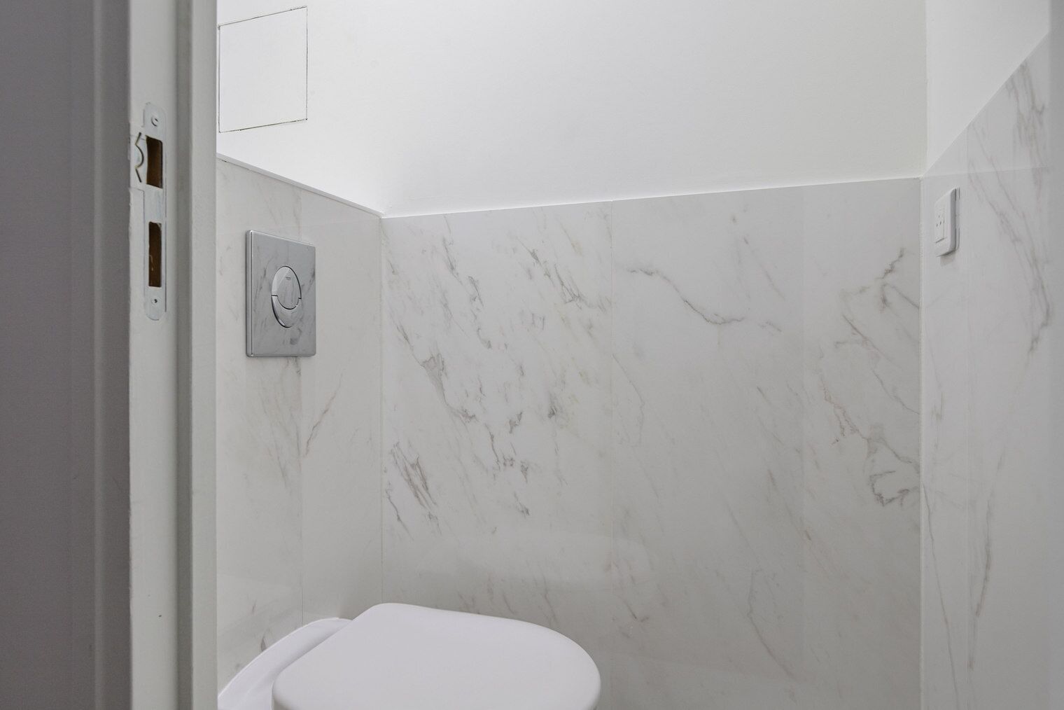A bathroom with a toilet, a wall-mounted control panel, and marble-patterned walls.