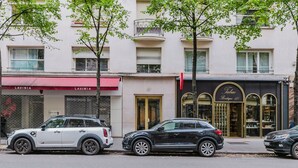 En gade med parkerede biler og butiksfacader, herunder et smykkeforretning og en restaurant.