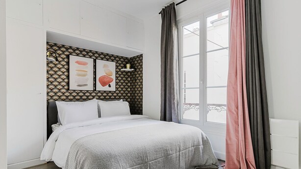 A bedroom with a bed, a window with curtains, and a wall with patterned wallpaper and artwork. - Blueground | Champ de Mars, near Eiffel Tower (Paris)