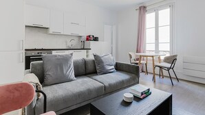 A modern living room with a grey sofa, a coffee table, and a dining area with a table and chairs. - Blueground | Champ de Mars, near Eiffel Tower (Paris)