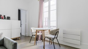 A modern, minimalist living room with a round table and two chairs, a grey sofa, and a white cabinet. - Blueground | Champ de Mars, near Eiffel Tower (Paris)