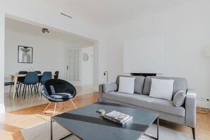 A modern living room with a grey sofa, a black chair, a coffee table, and a dining area with chairs and a table. - Blueground | Trocadero, washer, nr embassies (Paris)