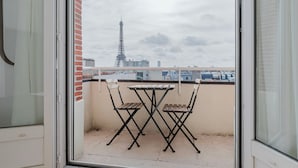 Un balcón con una mesa y sillas, vista de la Torre Eiffel y un paisaje urbano al fondo.