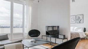 Una habitación de hotel moderna con un ventanal grande, un televisor de pantalla plana, un sofá, una mesa de comedor y una cama.