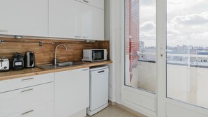 Cocina moderna con armarios blancos, encimera de madera, fregadero, microondas, hervidor y lavavajillas.