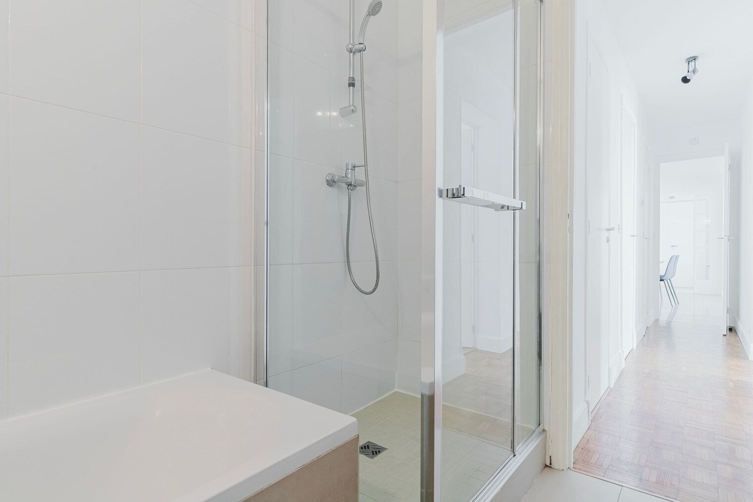 A modern bathroom with a glass shower enclosure, a white bathtub, and a hallway leading to another room.