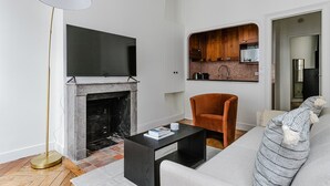 A modern living room with a fireplace, a flat-screen TV mounted above it, a sofa, a coffee table, and a floor lamp. - Blueground | Porte Dauphine, elev, nr metro (Paris)