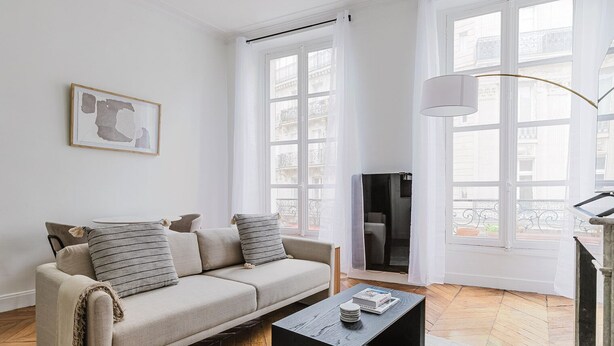 A living room with a sofa, a coffee table, and a TV. There are large windows and a view of buildings outside. - Blueground | Porte Dauphine, elev, nr metro (Paris)