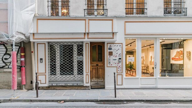 Une devanture de magasin avec une grille métallique, une enseigne et une vitrine où sont exposées des chaussures.