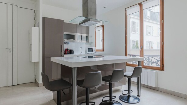 Eine moderne Küche mit Kochinsel, Barhocker und Blick durch ein großes Fenster nach draußen.