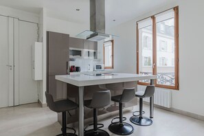 Et moderne køkken med en central ø, barstole og udsigt til det fri gennem et stort vindue.