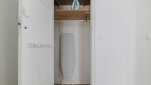 A room with a wooden floor, a white door, and a hanging garment steamer. - Blueground | Batignolles 2bd apartment (Paris)