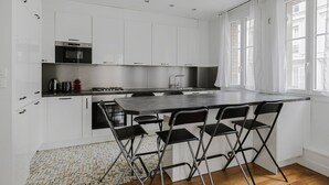 A modern kitchen with white cabinets, a black countertop, and a dining area with foldable chairs. - Blueground | Batignolles 2bd apartment (Paris)