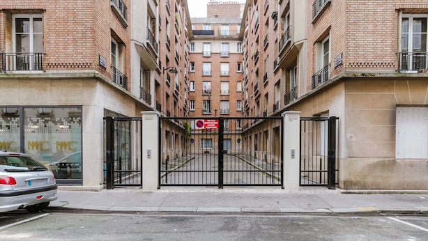 A gated entrance to a building with a brick facade and multiple windows. - Blueground | Batignolles 2bd apartment (Paris)