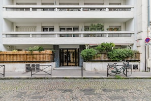Stylish building with balconies and a central entrance, featuring a glass door and greenery planters.